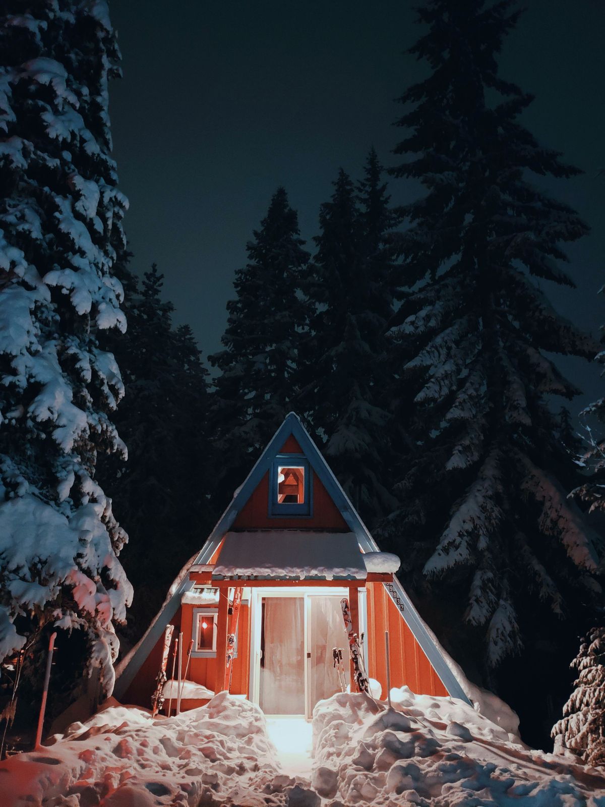 A-frame cabin glowing warmly between snow-covered evergreens at night