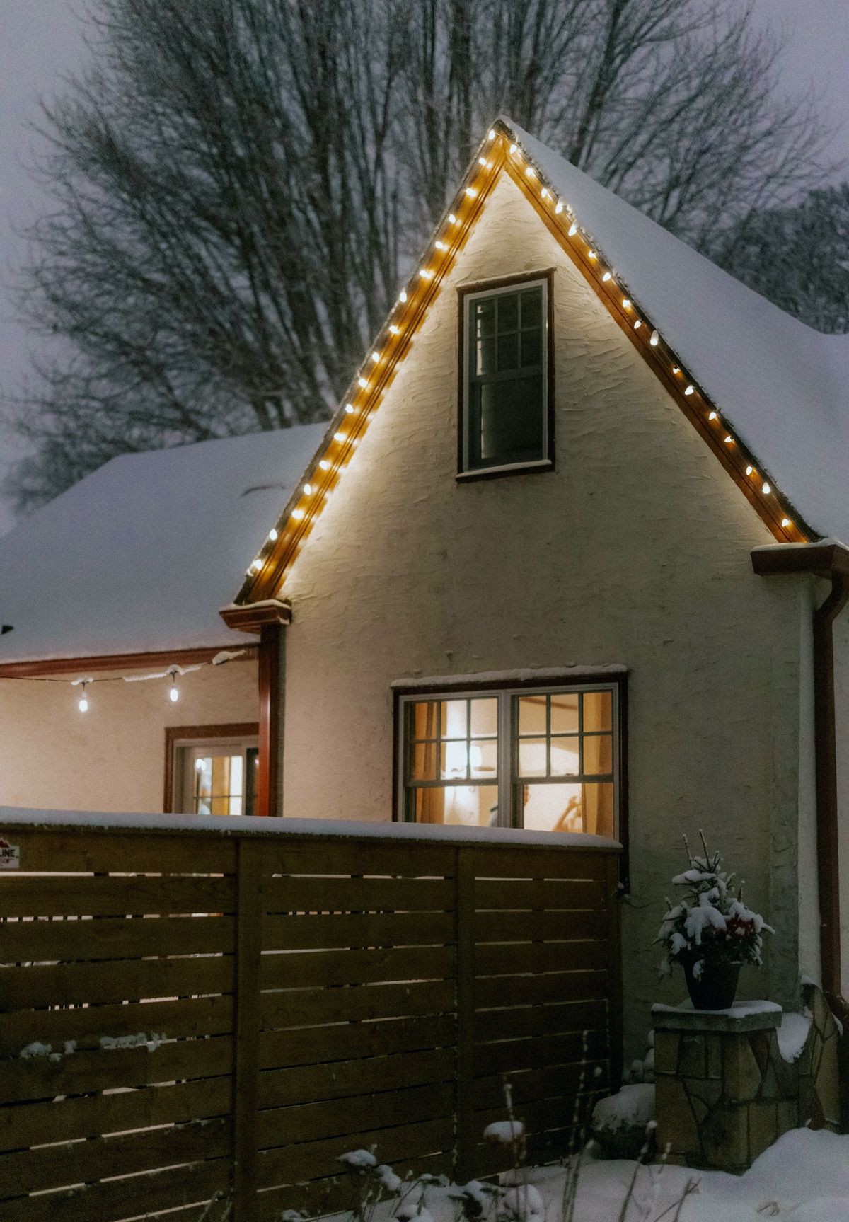 Snow-covered gable at dusk with evenly spaced warm white bulbs along the trim