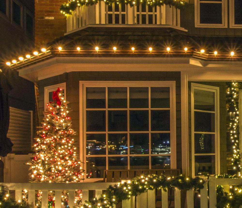 Bay window and balcony wrapped in lit garland beneath a traced roofline
