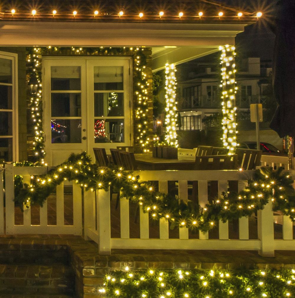 Porch columns wrapped in warm white lights with garland along the railing